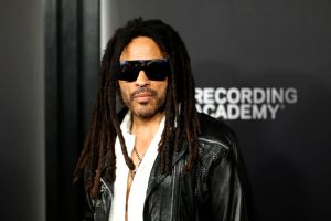 Lenny Kravitz wearing a white shirt and a black jacket and sunglasses on a red carpet