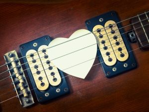 A heart-shaped guitar pick woven into guitar strings.