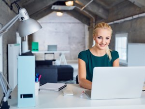 young woman smiling and typing on laptop in modern office