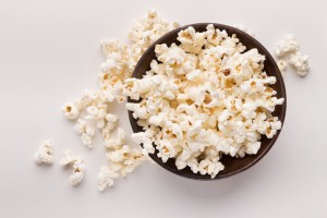 Wooden rustic bowl of popcorn isolated on white background, top view. Fast food, cinema snack and entertainment concept, cutout