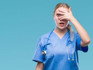 Young blonde surgeon doctor woman over isolated background peeking in shock covering face and eyes with hand, looking through fingers with embarrassed expression.