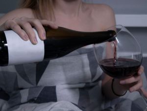 beautiful slender half-naked girl pours red wine from a bottle without a label into a huge glass and in bed