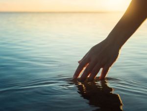 A female hand touching the ocean water in front of a beautful sunset during summer time., peaceful concept