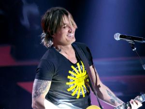 Keith Urban on stage playing guitar in a black t-shirt.