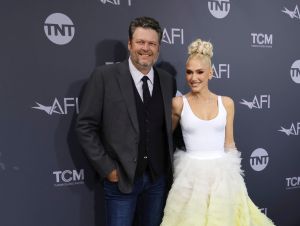 Blake Shelton in a blue blazer and tie, and Gwen Stefani next to him in a white and green dress.