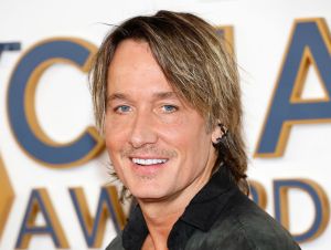 Keith Urban is posing in a black shirt on the CMA red carpet.