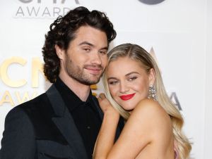 Kelsea Ballerini, in a pink dress, leaning on her boyfriend Chase Stokes in a black suit.