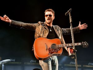 Eric Church is on stage wearing a leather jacket and holding a guitar.