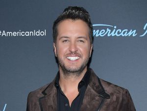 Luke Bryan is posing in a brown leather jacket and black shirt.