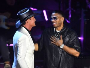 Tim McGraw is on stage in a white suit and cowboy hat, with Nelly dressed in black and sunglasses.