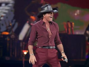 Tim McGraw is on stage in a black cowboy hat and a maroon shirt and pants.