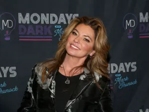 Shania Twain posing in a black top and a black and silver jacket.