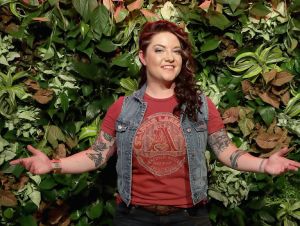Ashley McBryde in a red t-shirt and denim jacket posing with her hands held out.