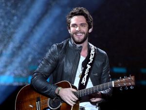 Thomas Rhetts music video - Thomas is on stage playing guitar in a black jacket.