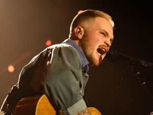 Zach Bryan's Brooklyn concert - Zach is on the stage singing and wearing a blue and green shirt.