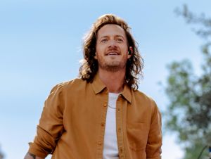 Tyler Hubbard's Solo Career - Tyler is in a brown jacket and white t-shirt outside smiling.