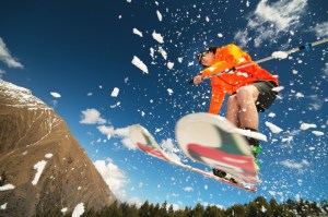 Man skier in flight after jumping from a kicker in the spring against the backdrop of mountains and blue sky. Spring skiing in Pocono Pennsylvania.