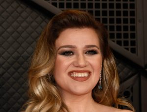 Kelly Clarkson attends the 66th GRAMMY Awards smiling wearing a white strapless gown, Kelly Clarkson Files New Lawsuit In Legal War With Ex-Husband.