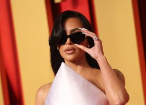 Kim Kardashian attends the 2024 Vanity Fair Oscar Party holding her sunglasses white wearing a pointy white dress, Kim Kardashian Sued Over Having Furniture Knockoffs.