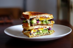 A breakfast sandwich with egg and avocado on a white plate with blurred background. The best breakfast sandwich in Massachusetts is at Mike and Patty's.