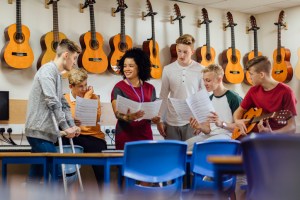 Students are in a music lesson at school. They are discussing sheet music with their teacher.