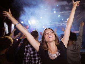 Young woman with arms raised enjoying at nightclub during music festival, concert