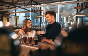 Young man and woman at the bar with different types of beers. Couple at brewery bar and tasting beers.