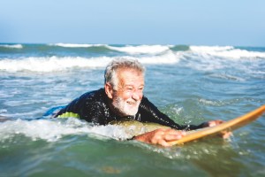 A senior man on a surfboard attending surf camp.