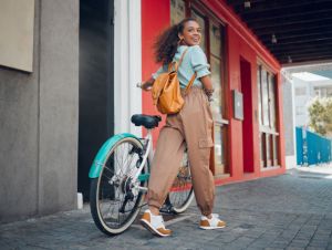 Happy, city and girl with a bicycle to travel to school, university or college to reduce carbon footprint outdoors. Smile, street and young student traveling or riding a cool bike in an urban town