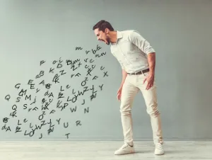 Handsome angry man is yelling and the stream of words going out of his mouth, on gray background, swearing concept