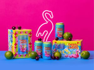 Blake’s Hard Cider Cherry Limeade, cans, cartons, and cherries, with LED flamingo on pink and blue background.