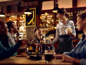 Happy waitress serving hamburger with French fries to group of guests in a bar, dining out concept