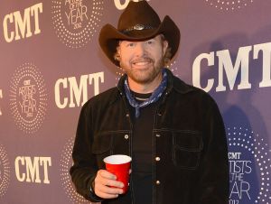 CMT Will Pay Tribute To Toby Keith - Toby wearing a black shirt and cowboy hat and holding a red solo cup on a CMT red carpet.