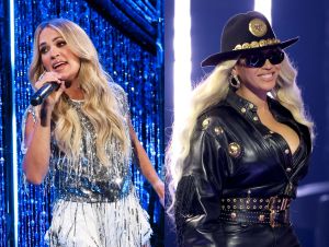 Carrie Underwood Loves Beyonce—Carrie is in a stylish silver outfit with a mic, and Beyonce is in a black outfit with a cowboy hat and sunglasses.