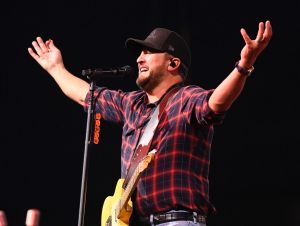 Luke Bryan Reveals What He's Most Proud Of - Luke on stage in a ball cap and red plaid shirt.