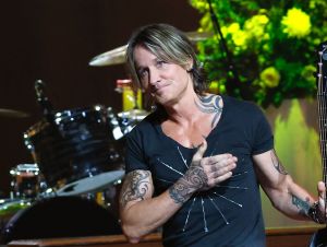 Keith Urban Mega Mentor - Keith is on stag in a black shirt holding his hand to his heart.