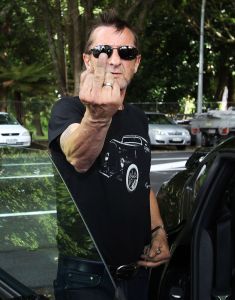 AC/DC drummer Phil Rudd gestures to members of the media after leaving Tauranga District Court