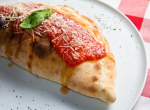 A calzone in New Jersey at a restaurant on a plate with red sauce on top.