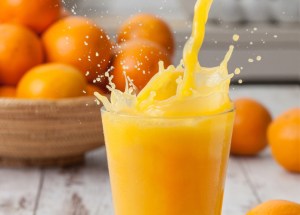Pouring a glass of orange juice creating splash, creating a splash with oranges in a bowl. The best juice.