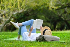 Happy woman lying on green grass reading a book in the park( outdoors ). Book lovers