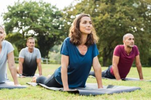 A group of people doing yoga on mats outdoors on the grass. Boston Seaport Sweat begins May 1.