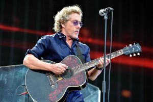 Roger Daltrey performing on stage and playing an acoustic guitar.