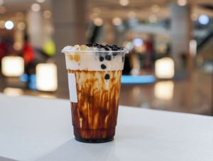 A plastic cup of fresh milk and brown sugar syrup, topped with boba or bubble tapioca pearl on white table.