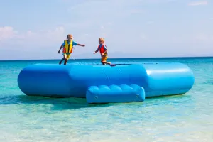 Kids jumping on trampoline on tropical sea beach. Children jump on inflatable water slide. Aqua amusement park in exotic island resort. Family vacation with outdoor amenities.