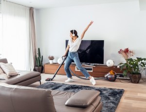 Young happy woman listening and dancing to music while spring cleaning the living room floor with a vacuum cleaner