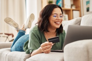 Relax, laptop and credit card, happy woman on couch in living room for internet banking in home for online shopping. Ecommerce payment, smile and cashback, girl on sofa with computer and website sale