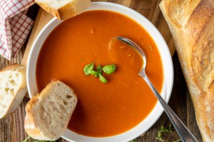 Homemade tomato soup with baguette on a deep plate with spoon on wooden table background. The best places to get tomato soup in Massachusetts.
