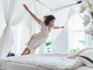Woman jumps on the hotel bed as if in flight.