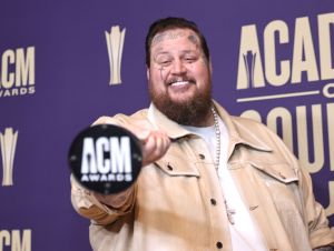 Jelly Roll in a tan jacket holding an acm award.