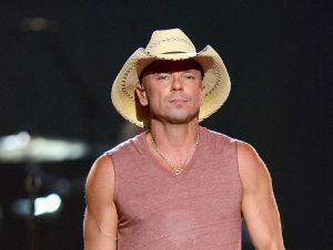 Kenny Chesney Praises His Mom Karen  - Kenny on stage in a cowboy hat and red tank top.